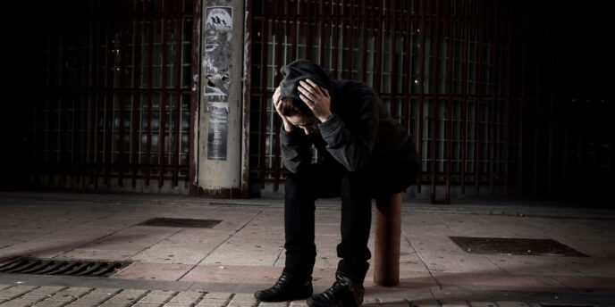 person dressed in black sitting in the dark on a sidewalk hanging their head while wondering about buprenorphine and overdose