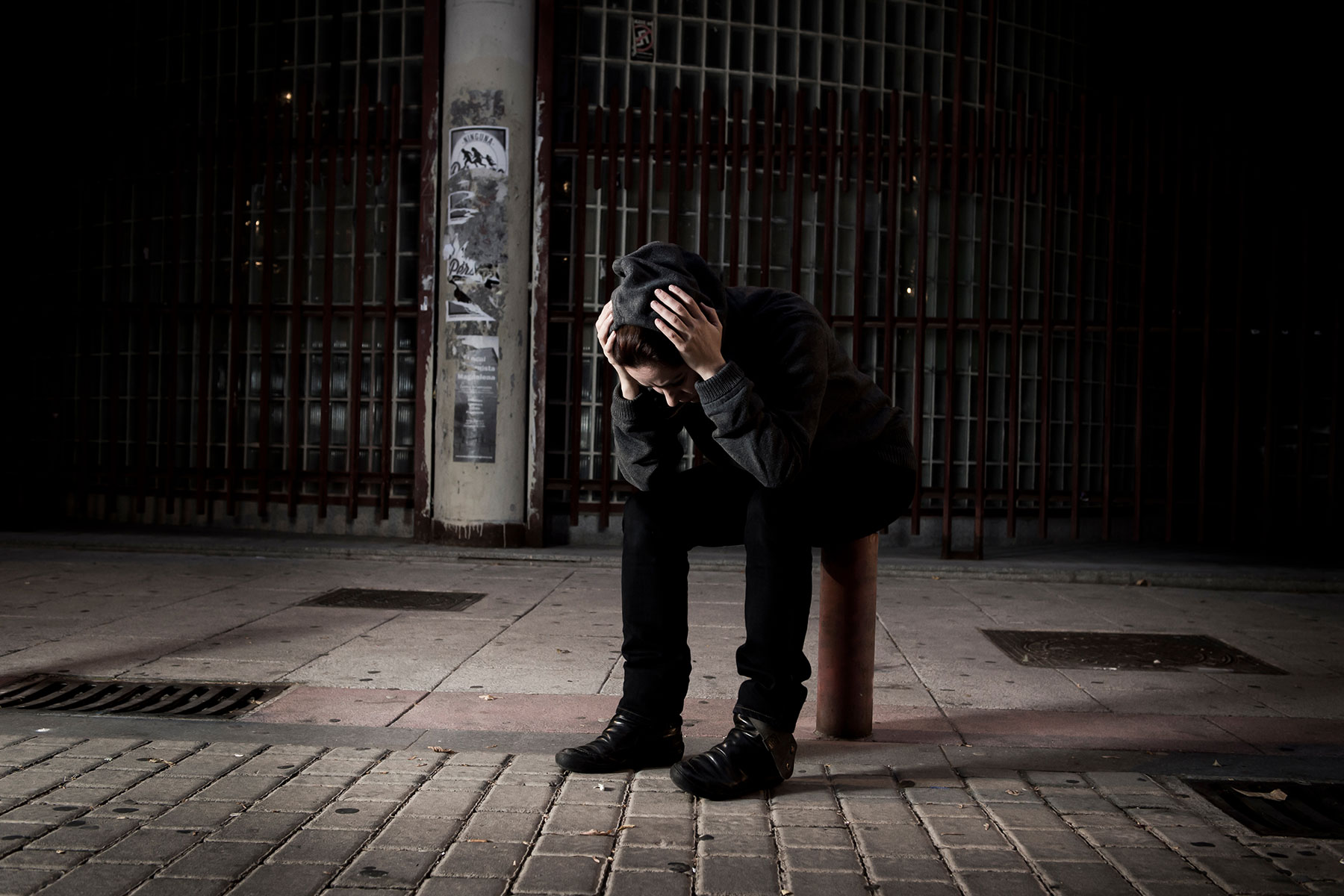 person dressed in black sitting in the dark on a sidewalk hanging their head while wondering about buprenorphine and overdose