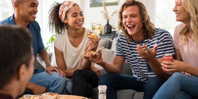group of friends on couches around pizza celebrating national recovery month