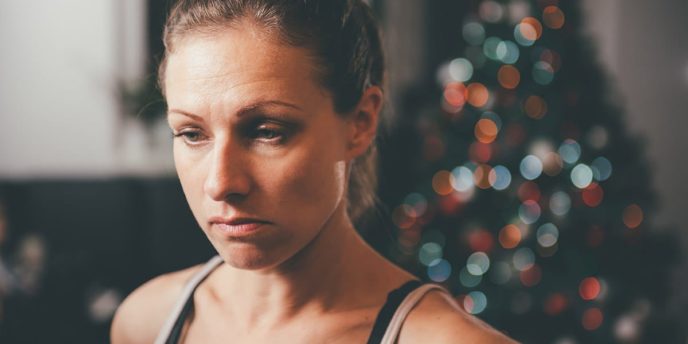 woman in front of christmas tree considers dealing with addiction triggers during the holidays