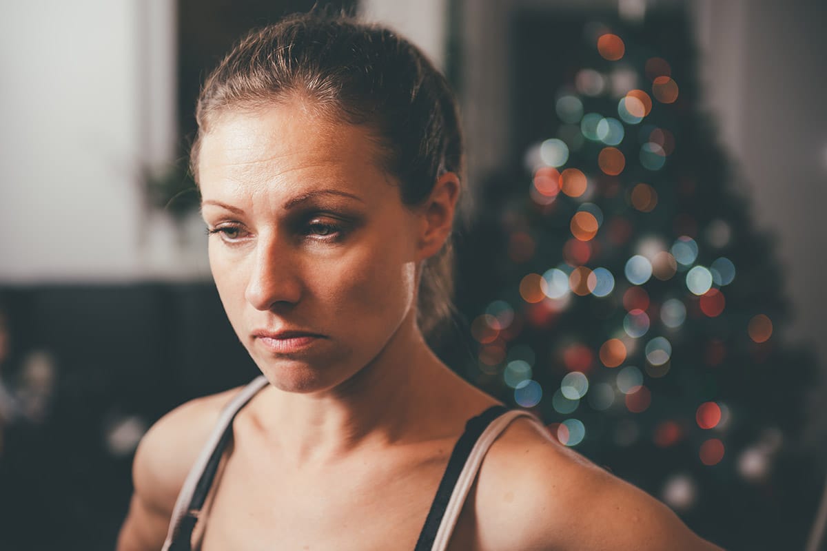 woman in front of christmas tree considers dealing with addiction triggers during the holidays