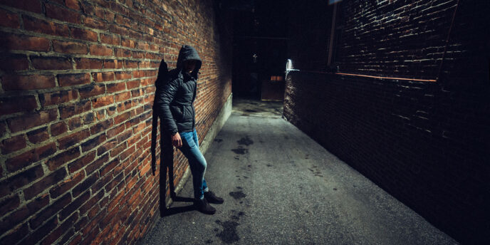 person in hoodie leaning against brick wall of dark alleyway while pondering the question what are the most dangerous drugs