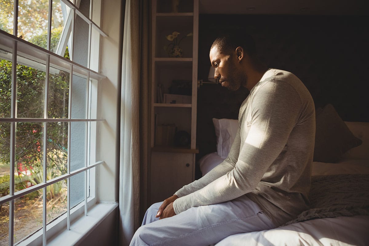man sits in front of window and considers what does heroin withdrawal feel like