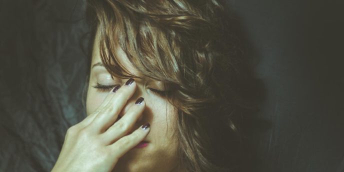 Woman with eyes closed and her hand on her face looking distressed while considering how alcohol affects your body