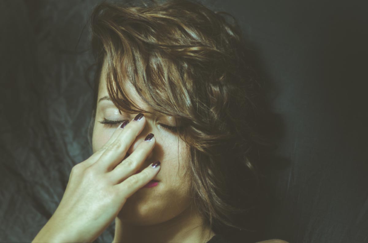 Woman with eyes closed and her hand on her face looking distressed while considering how alcohol affects your body
