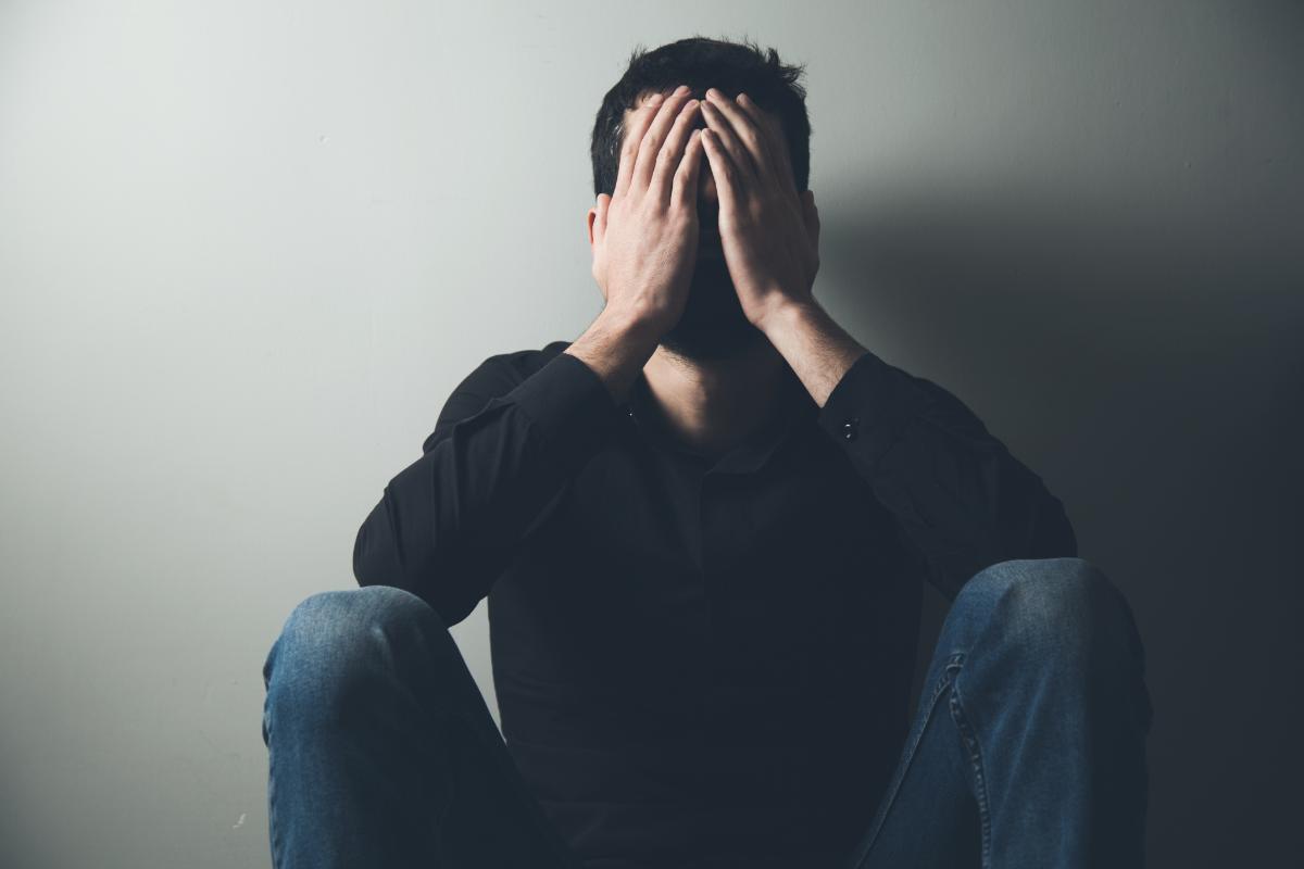 Man sitting against wall covering his face with his hands wondering if naloxone will cause withdrawal