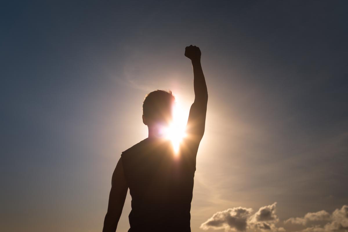 Person triumphantly holding up arm against a sunny backdrop after learning how to stay motivated to staying sober
