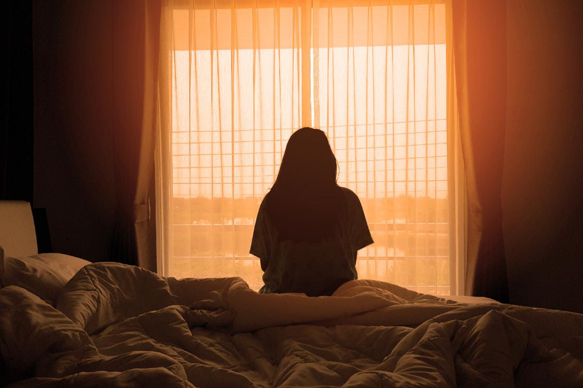 Woman sitting on the edge of bed looking out window while contemplating the question what do stimulants do to the brain
