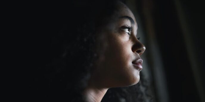 person in dark room looking out window while worrying about the dangers of flakka