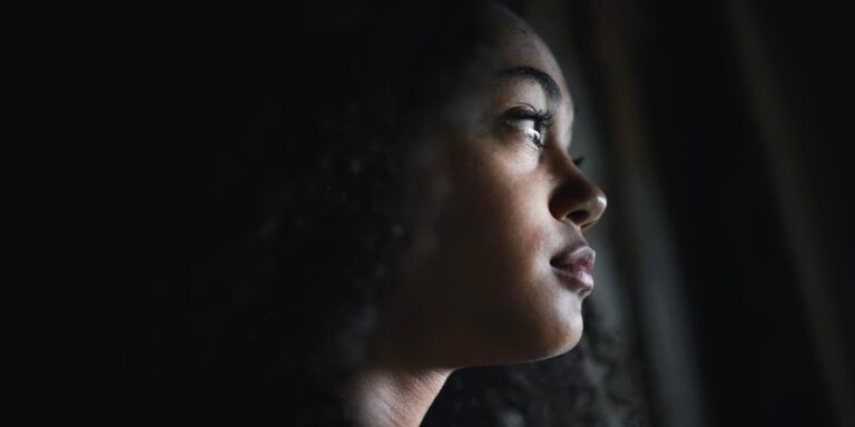 person in dark room looking out window while worrying about the dangers of flakka