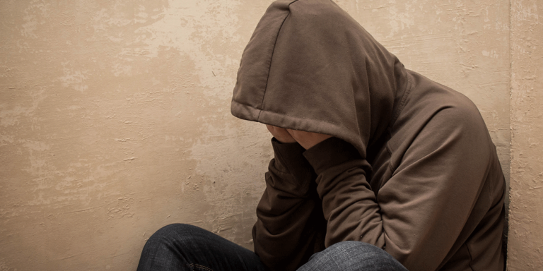 Man in hoodie sitting against wall with head in hands thinking about answers to the question what are oxycodone withdrawal symptoms